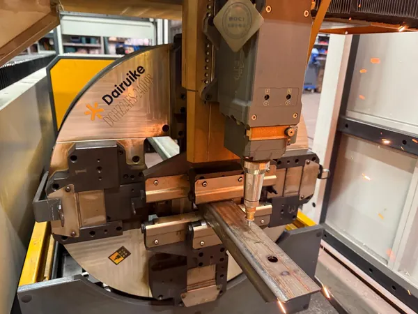 Laserkopf bearbeitet ein rechteckiges Metallprofil in einer Spannvorrichtung.